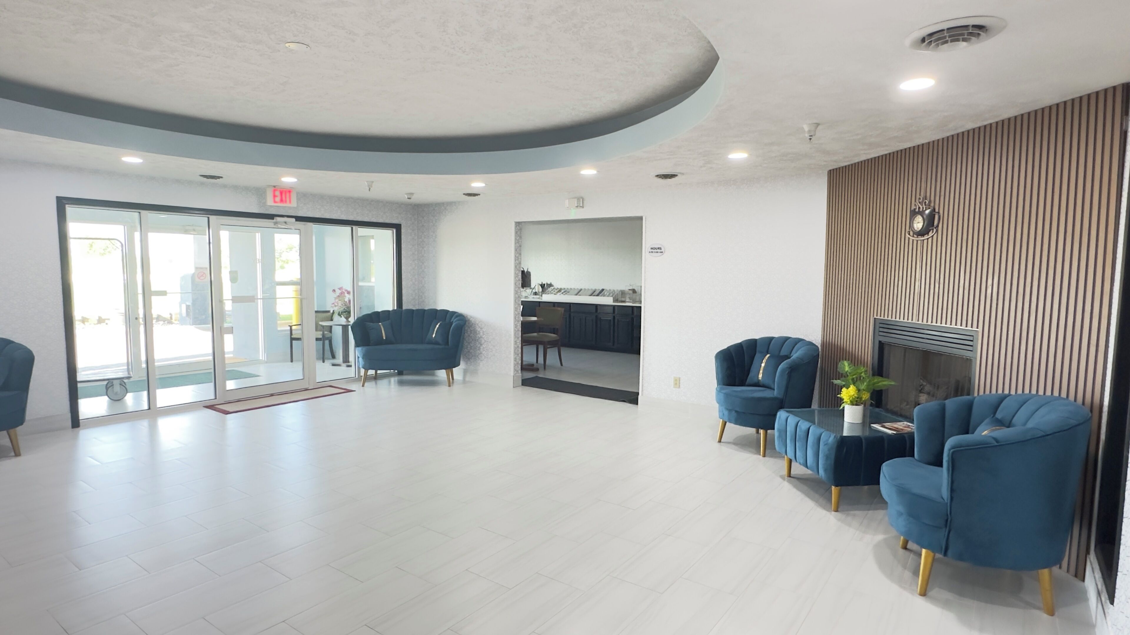A modern hotel lobby with a curved ceiling, a glass door entrance, a dining area, and blue armchairs.