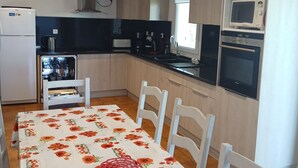 A compact kitchen with a refrigerator, microwave, and oven. A dining table with chairs is placed in the center. - Detached house 90m south facing for 6 people with air conditioning (Bauduen)