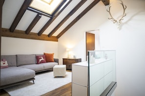 Ein modernes Wohnzimmer mit einer Loft-Decke, einer Couch mit Dekokissen, einer Glaskonsole und einem Holzboden.