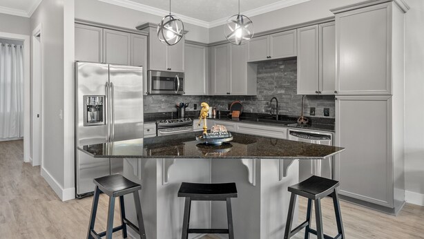 A modern kitchen with stainless steel appliances, a granite island, and bar stools. - Pirate's Pearl | Pool | Balcony | Steps to Beach (Panama City Beach)