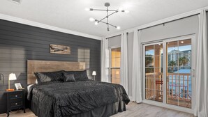 A bedroom with a large bed, a nightstand, a modern chandelier, and a sliding glass door leading to a balcony. - Pirate's Pearl | Pool | Balcony | Steps to Beach (Panama City Beach)