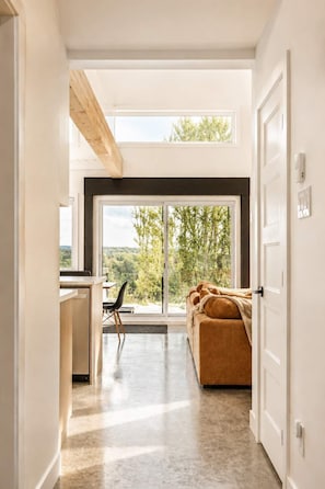 A modern interior with a kitchen area, a sofa, and a large window with a view of greenery. - Spa | Relaxation Net | Le Dormëa (Saint-Côme)