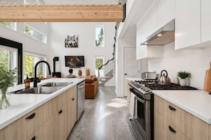 A modern kitchen with a central island, stainless steel appliances, and a dining area with a sofa. - Spa | Relaxation Net | Le Dormëa (Saint-Côme)