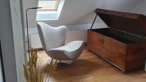 Ein Zimmer mit schrägem Dach, einem Oberlicht, einem modernen Sessel, einer Holzkommode und einer Topfpflanze.