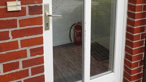 Eine Glastür mit weißem Rahmen, ein Feuerlöscher und eine Ziegelwand.