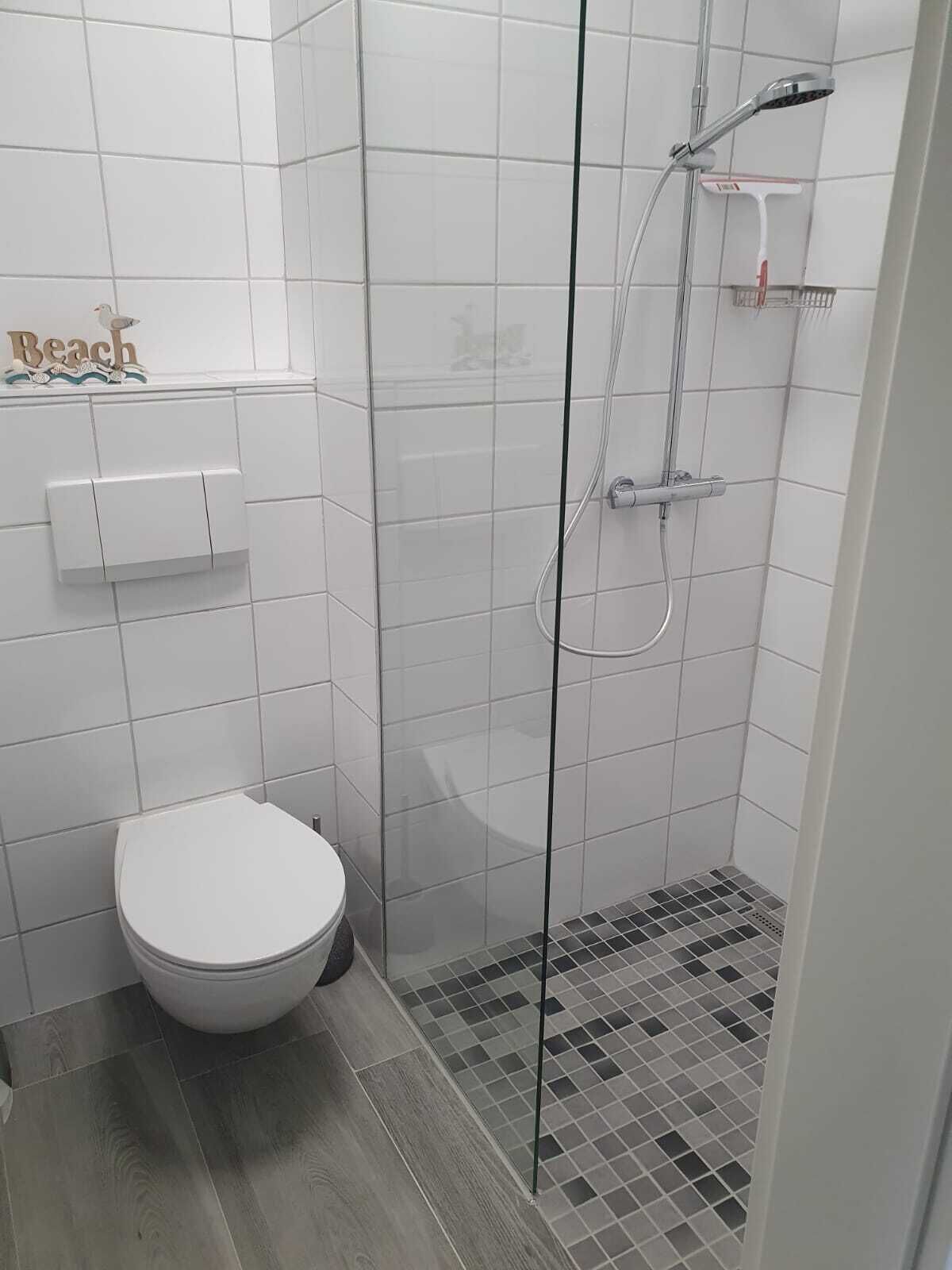 A small, modern bathroom with a glass-enclosed shower, a toilet, and a small shelf with a towel.