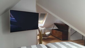 Ein Schlafzimmer mit einem Bett, einem an der Wand befestigten Fernseher, einer Holzkommode und einem Sessel.