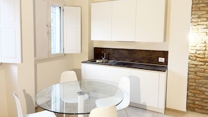 A modern kitchen with white cabinets, a glass dining table, and a stone accent wall.