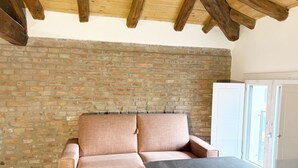 A room with a brick wall, wooden beams, a sofa, a table, and a door.