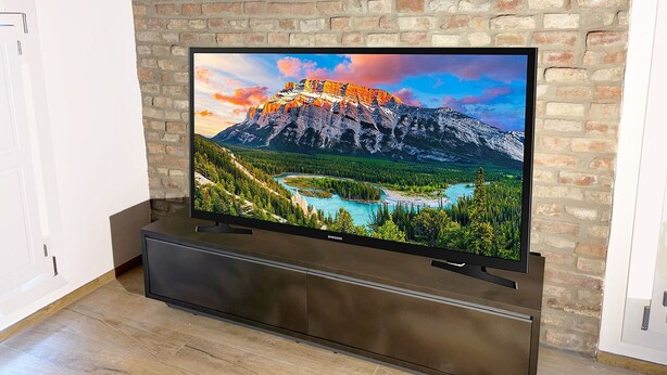 A flat-screen TV mounted on a brick wall with a wooden floor.