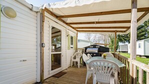 A covered deck with a grill, white chairs, and a table.