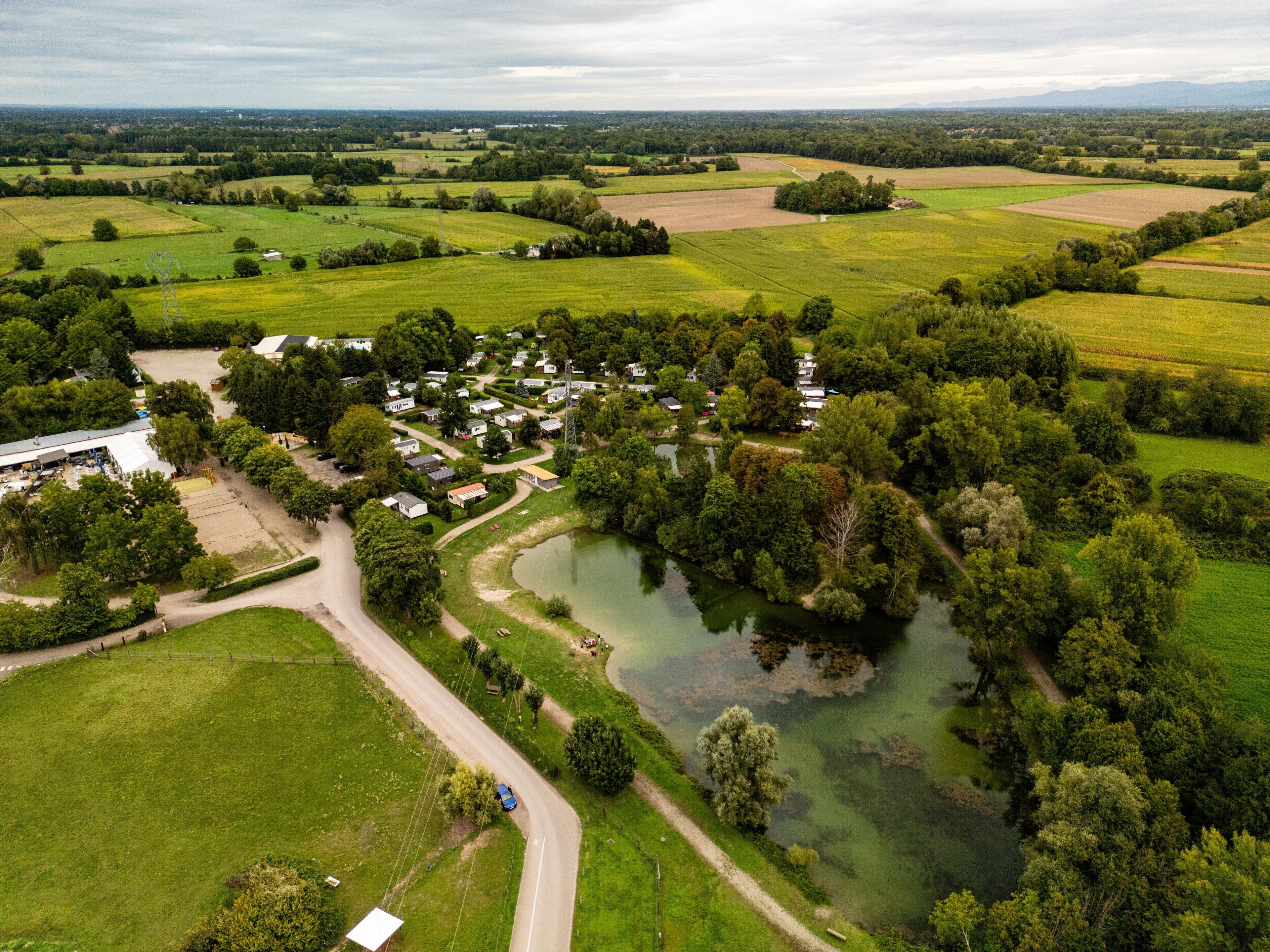 Luchtbeeld van een landelijk gebied met een groep huizen, een vijver en omliggende velden.