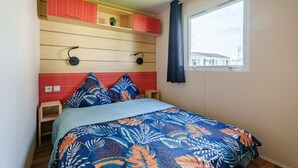 A bedroom with a bed, a window, a shelf with a plant, and a red cabinet.