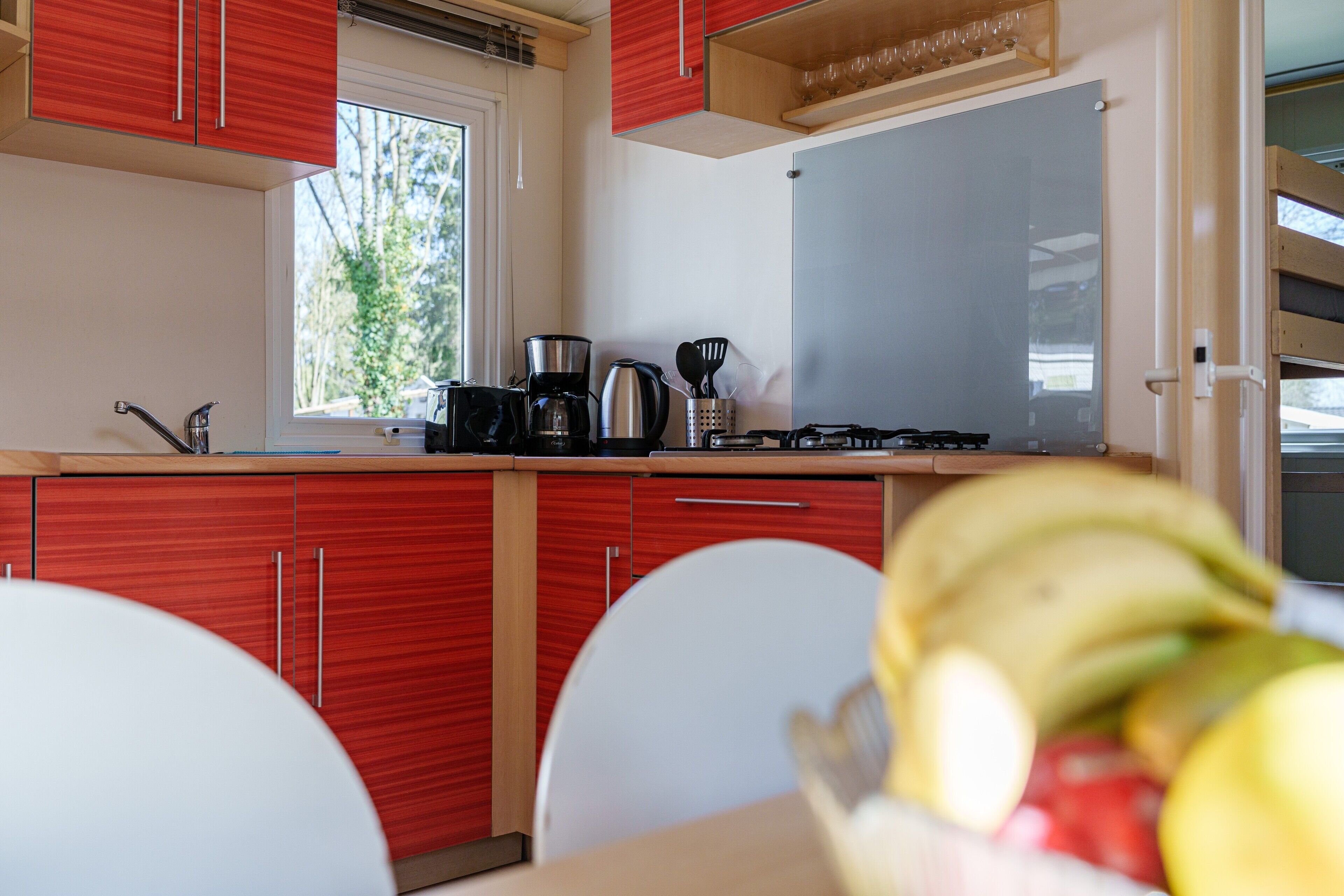 A kitchen with red cabinets, a window, a stove, and a coffee maker.