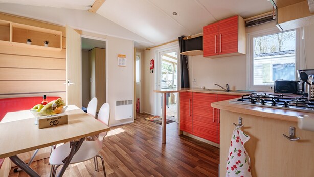 A kitchen with a wooden table, chairs, a gas stove, and red cabinets.