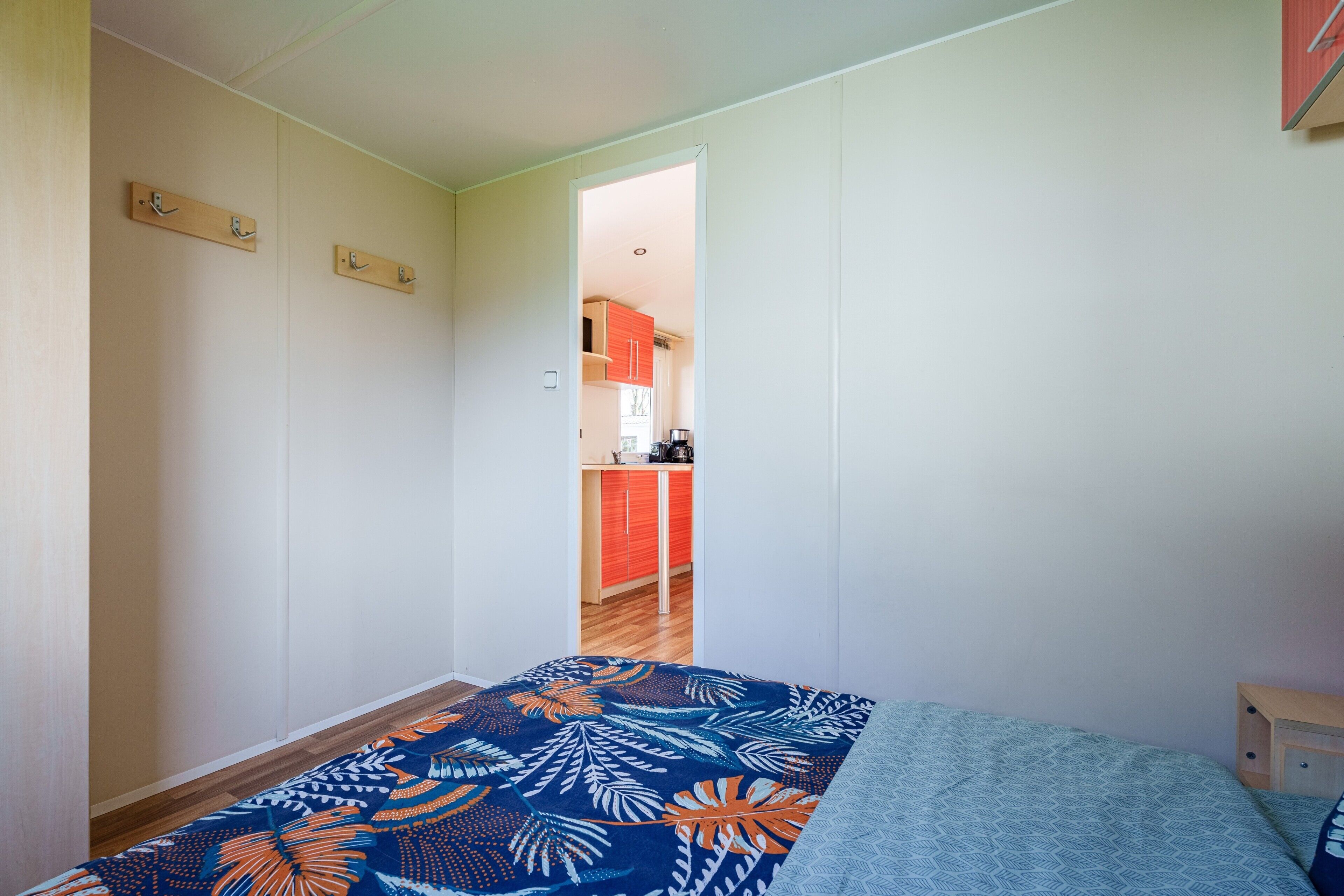 A bedroom with a bed, a wooden nightstand, and a door leading to a kitchen.