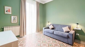 Una stanza con un divano grigio, due tavolini con lampade, un termosifone e piastrelle a motivi decorativi.