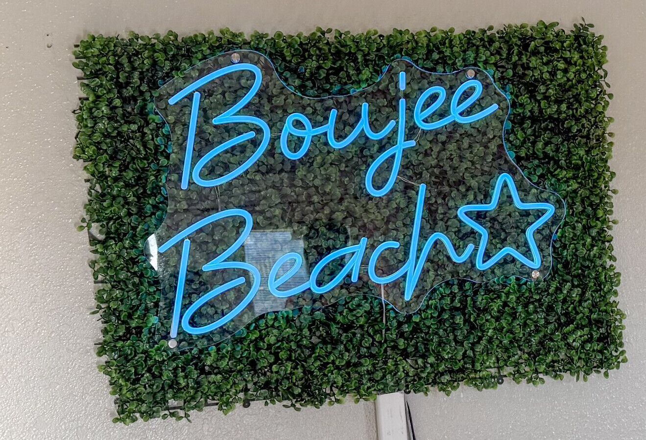 Un letrero de neón con el texto 'Boyee Beach' sobre un fondo de follaje verde.