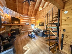A cozy log cabin interior with a fireplace, a sofa, a coffee table, and a staircase. - Boujee Bear- Modernized Cabin Minutes to Dollywood (Sevierville)