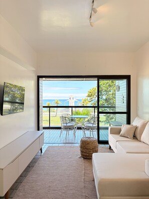 Sala de estar moderna com uma grande porta de correr de vidro que dá para uma varanda com vista para o mar e uma torre ao longe.