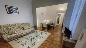 Olohuoneessa on kuviollinen sohva, roomalaisilla numeroilla koristeltu sohvapöytä, puinen TV-taso ja taustalla ruokailutila.