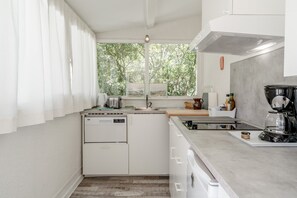 A compact kitchen with a dishwasher, a coffee maker, and a window with a view of trees. - Cottage 'La Petite Cadenelle' with Private Pool, Wi-Fi and Air Conditioning (Eygalières)