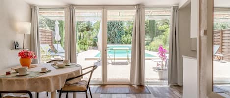 Une pièce comprenant une table à manger, des chaises, une lampe et donnant sur une piscine extérieure.