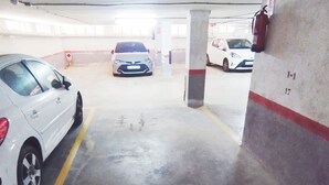 Een parkeergarage met betonnen pilaren, aangeduide parkeerplaatsen en een brandblusser bevestigd aan een pilaar.