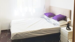 Slaapkamer met een bed, nachtkastje, lamp, plafondventilator en raam met gordijnen.