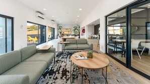 Ein moderner Arbeitsraum mit einem grünen Sofa, einem runden Holztisch und einem gemusterten Teppich.