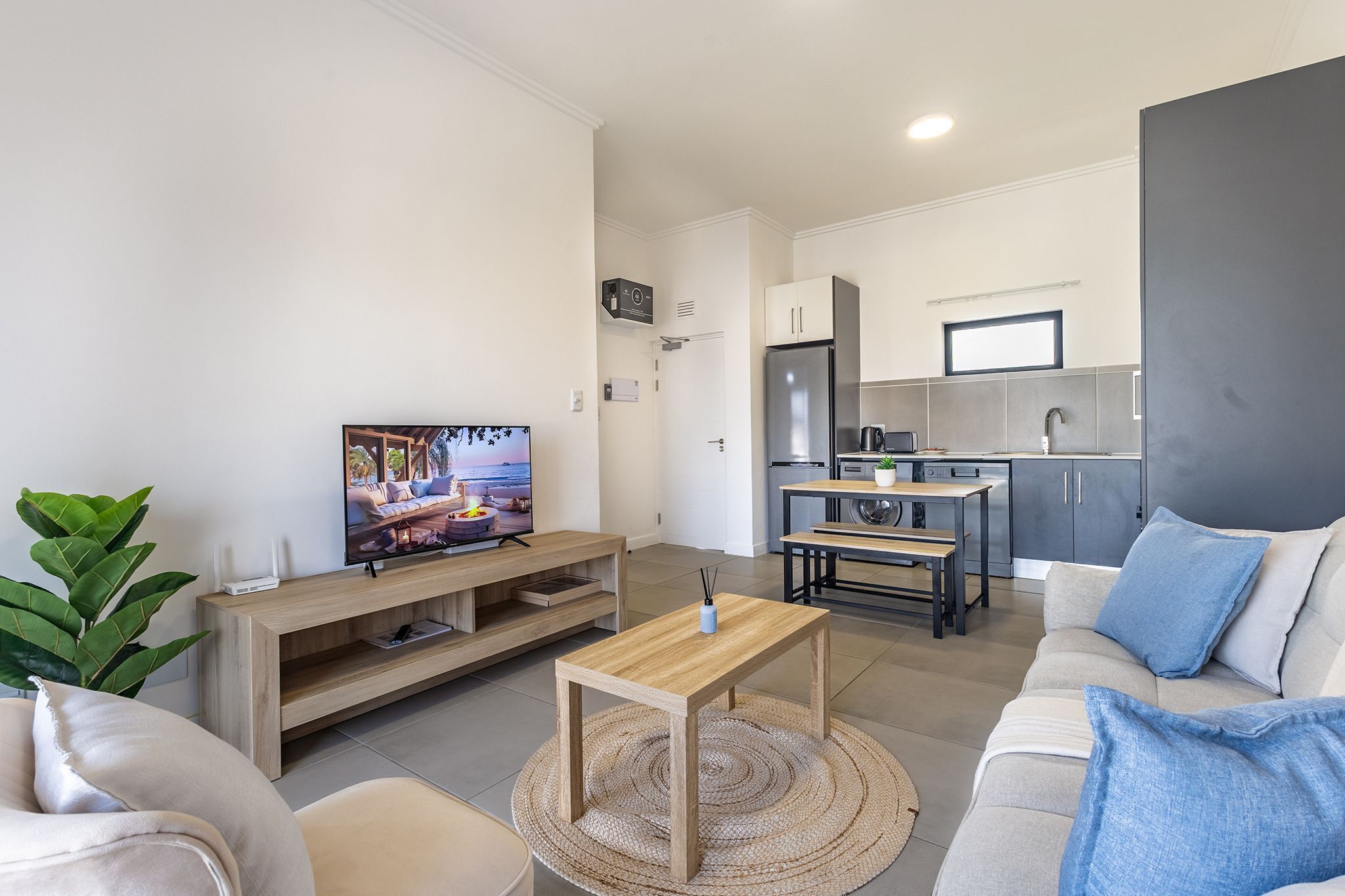A modern living room with a TV, sofa, coffee table, and a kitchen area with cabinets and a refrigerator.