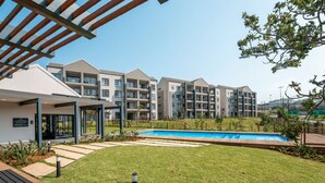 Ein modernes Apartmenthaus mit Schwimmbad, Sitzgelegenheiten im Freien und einem gepflegten Rasen.