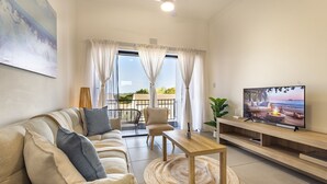 Ein modernes Wohnzimmer mit einer Couch, einem Fernseher und einem Balkon mit Vorhängen.