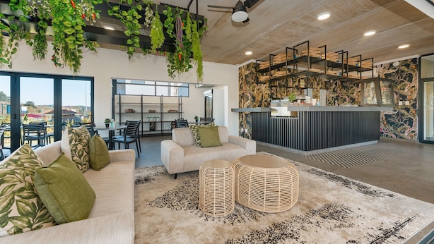 Ein modernes Interieur mit einer Couch, zwei runden Korbstühlen und einem Deckenventilator, ergänzt durch hängende Pflanzen.