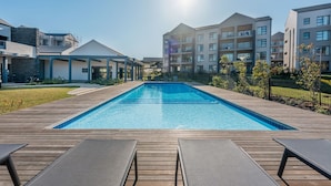 Ein moderner Wohnkomplex mit zentral gelegtem Schwimmbecken, einer Holzterrasse und Liegestühlen.