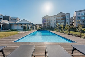 Ein moderner Wohnkomplex mit zentral gelegtem Schwimmbecken, einer Holzterrasse und Liegestühlen.