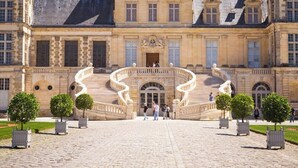 A grand building with a central staircase leading to a door, surrounded by symmetrical landscaping and a cobblestone pathway. - Chateau Walk One Bedroom (Fontainebleau)