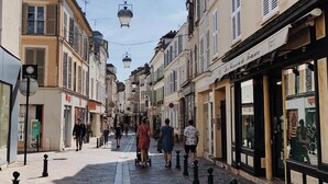 A narrow street lined with buildings, some with shops and signs, and a few pedestrians walking. - Chateau Walk One Bedroom (Fontainebleau)