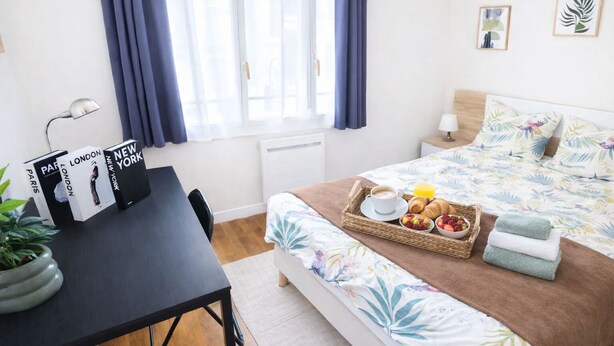 A neatly arranged bedroom with a bed, bedside table, and a desk with books. - Chateau Walk One Bedroom (Fontainebleau)