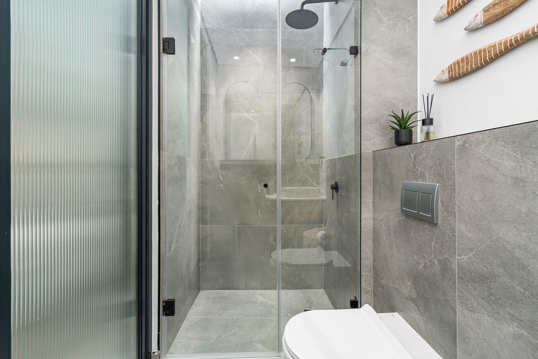 A modern bathroom with a glass-enclosed shower, a white toilet, and a marble-tiled wall.