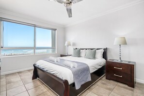 Une chambre à coucher comprenant un lit, des tables de chevet, un ventilateur de plafond, une fenêtre avec vue et une lampe.