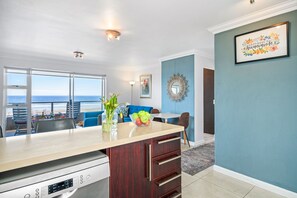 Une cuisine moderne dotée d’un grand îlot central, d’un coin repas offrant une vue agréable et d’un salon agrémenté d’un mur d’accent bleu.