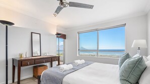 Ein Schlafzimmer mit einem großen Bett, einem Schreibtisch, einem Stuhl, einem Spiegel und Blick auf den Strand.