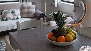 En matplats med ett bord dukat för två personer, en soffa och en stol. En skål med frukt står på bordet.