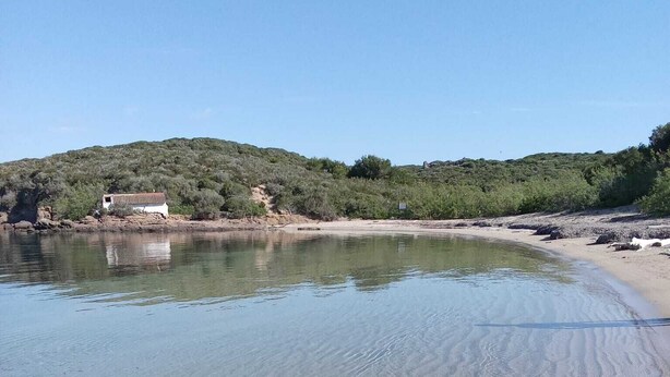 En strand med klart, grunt vatten, en sandstrand och en byggnad i bakgrunden.