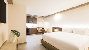 A modern hotel room with a large bed, a desk with a chair, a small kitchen area, and a flat-screen TV mounted on the wall. - Magdalena 1163 (San Juan)