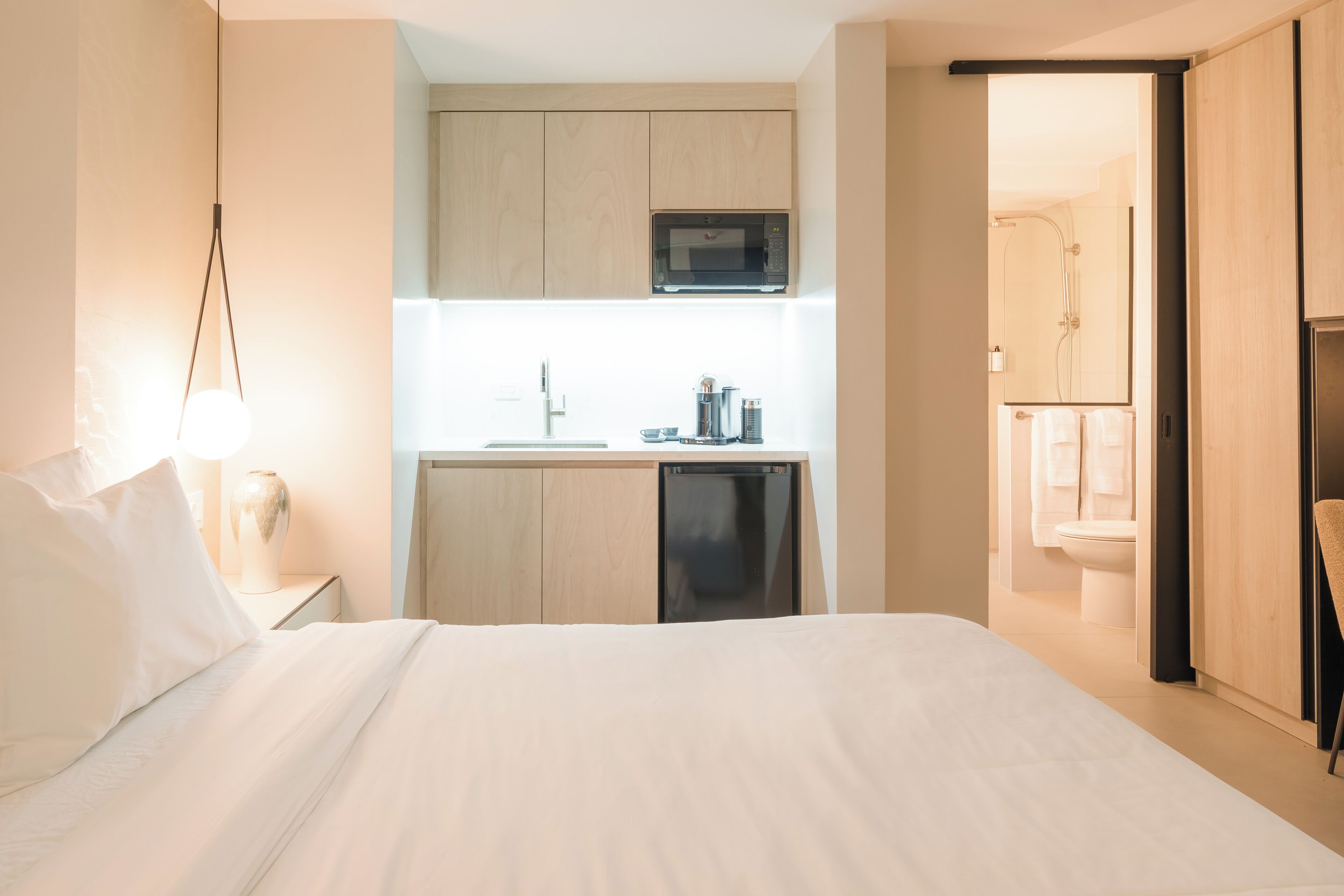A hotel room with a bed, a small kitchenette with a microwave, and a bathroom with a shower and toilet.
