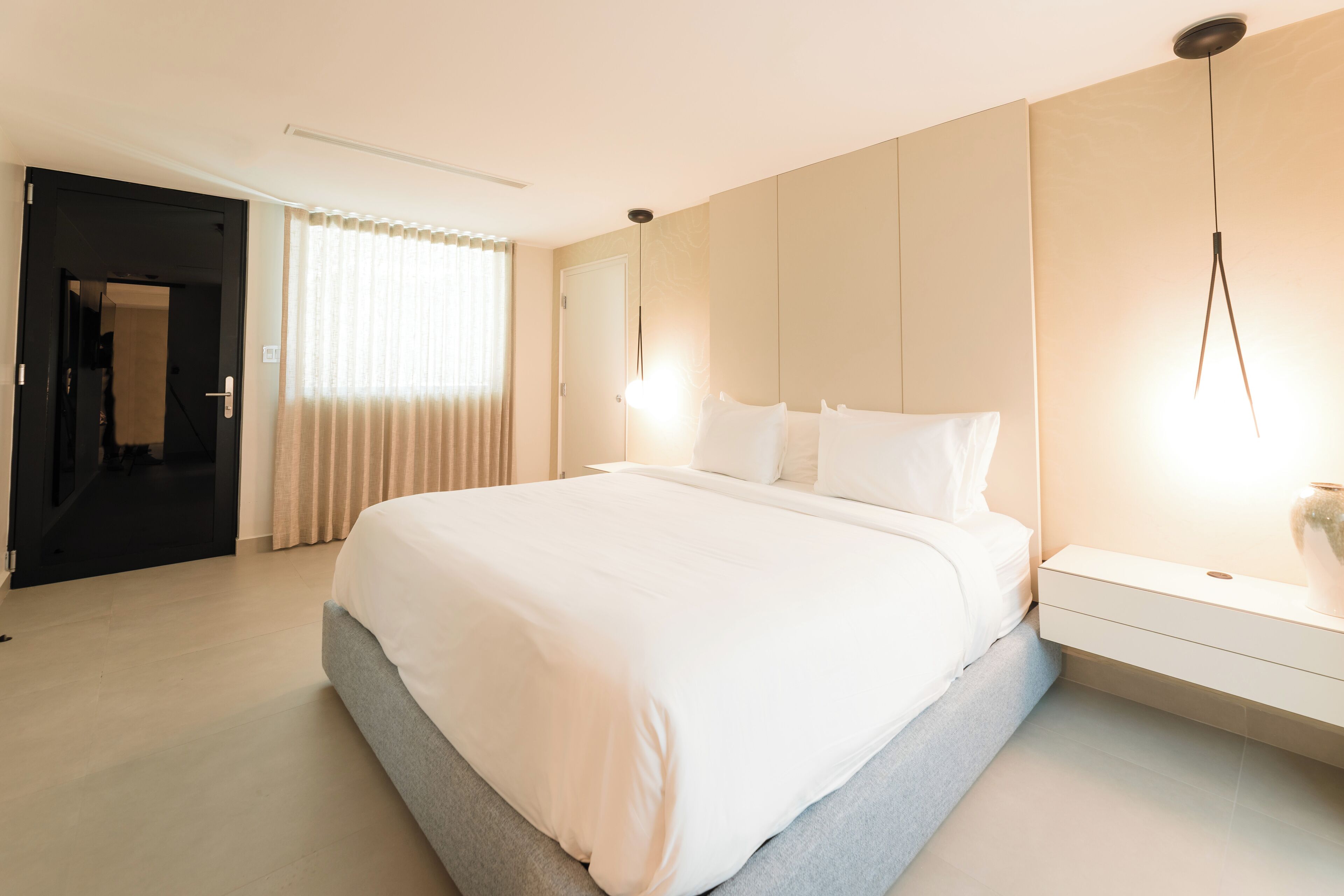 Un dormitorio de hotel moderno con una cama grande, mesitas de noche y vistas al pasillo.