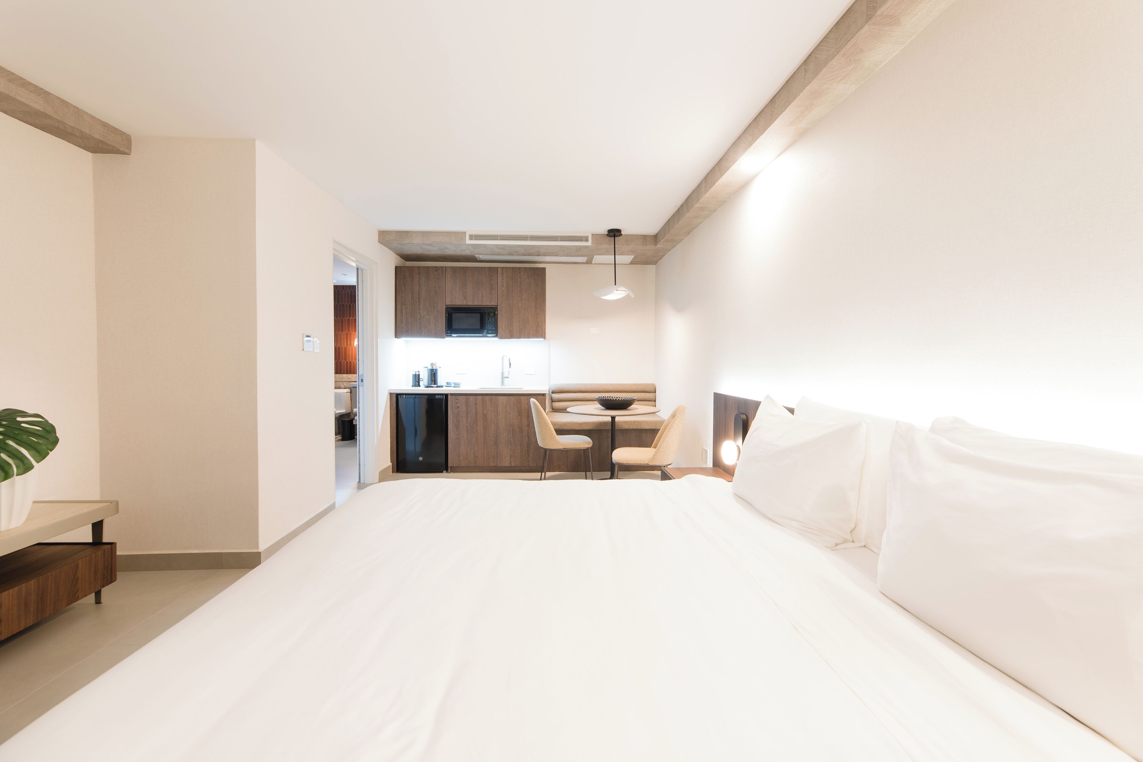 A modern hotel room with a large bed, a small kitchenette, and a seating area.