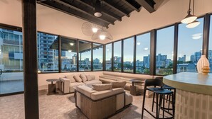 A modern interior with large windows, a sofa set, a bar area, and a city view. - Magdalena 1163 (San Juan)